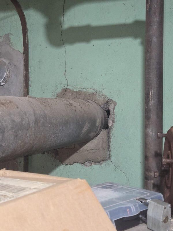 Conducted inspection of commercial boiler system showing extensive deterioration of pipe infrastructure. Documented severe corrosion at multiple connection points, including a compromised reddish valve assembly and significant mineral buildup at joints. Noted structural damage to wall penetration with visible cracking extending from pipe entry point, requiring both immediate repair options and complete system replacement alternatives for client consideration.