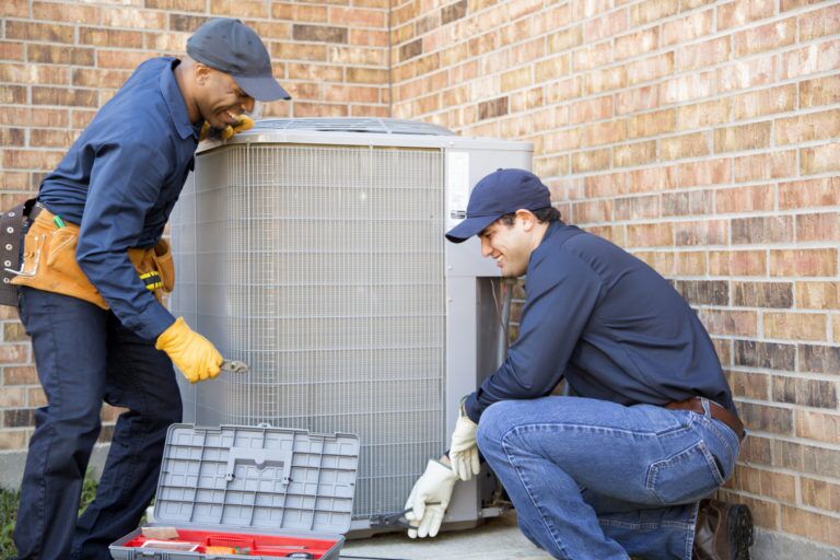 Gray air conditioning unit being replaced by two technicians.