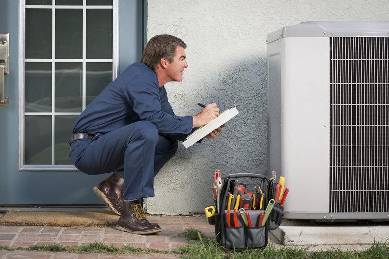 National Heating & Air Conditioning Technician repairing an AC unit and holding a checklist.